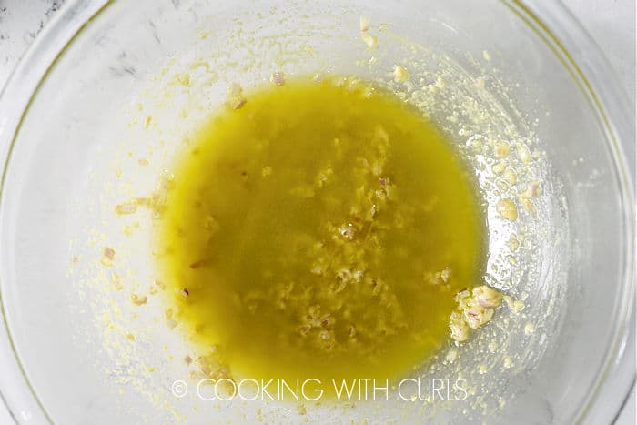 Mustard, oil and shallots mixed together in a glass bowl. 