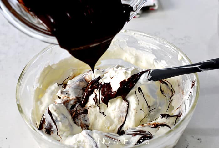 Pouring melted chocolate into the cream cheese mixture while stirring with a gray silicone spatula. 