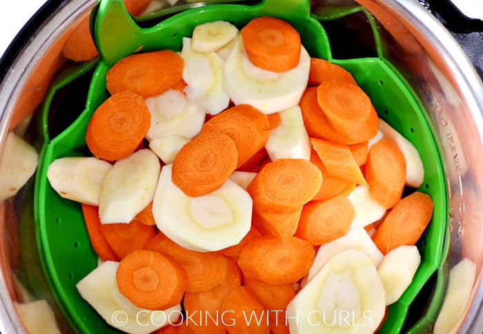 Raw, sliced carrots and parsnips in a green silicone strainer inside a pressure cooker. 