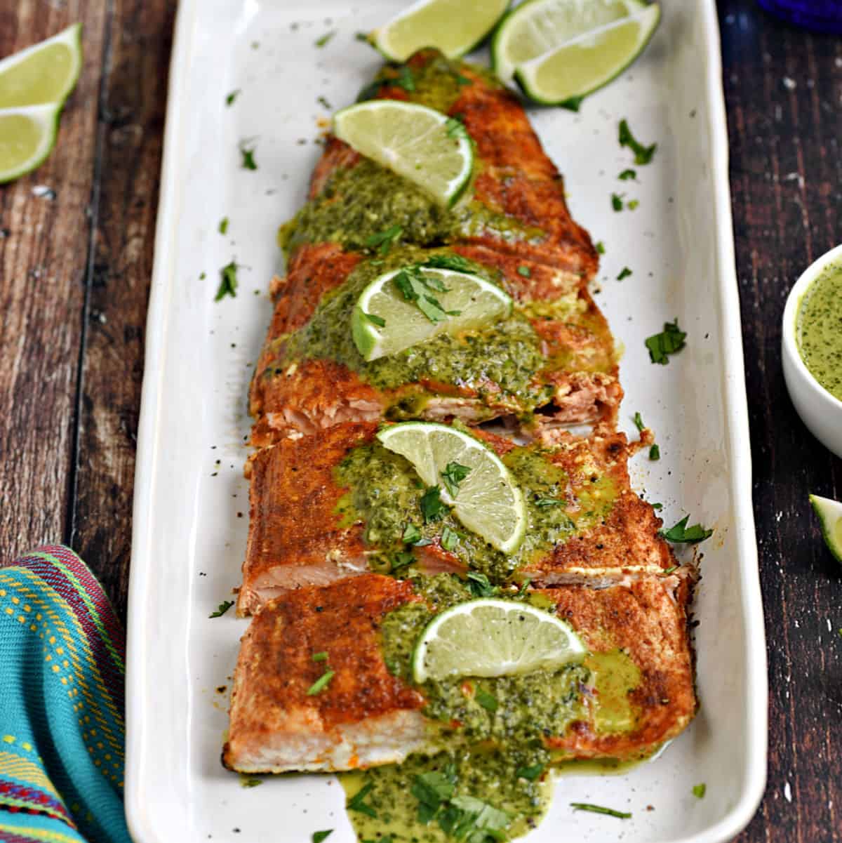 Baked salmon filet topped with cilantro sauce and lime wedges on a white platter.