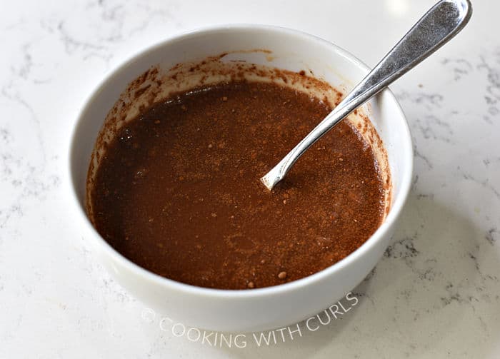 Beef stock mixed with spices and tomato paste in a small, white bowl. 