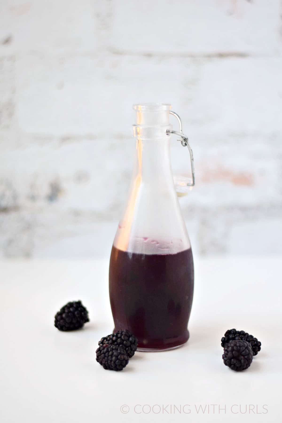 Blackberry syrup in a glass bottle with a swing top lid and fresh berries  scattered below.