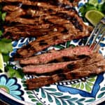 Grilled skirt steak on a platter with lime wedges and cilantro leaves.