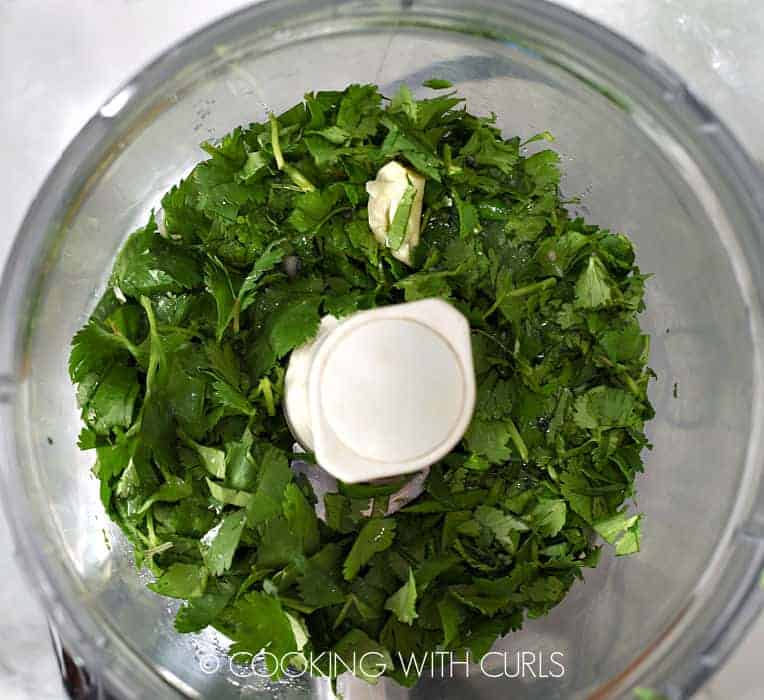 Cilantro, lime juice, garlic, and green onions in the bowl of a food processor. 
