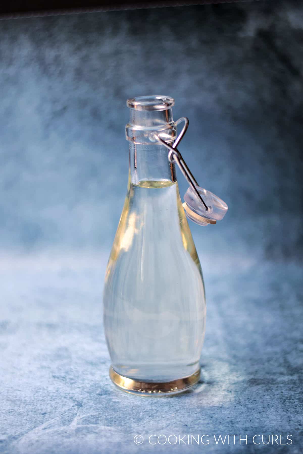 Clear simple syrup in a glass bottle with a blue sponged background.