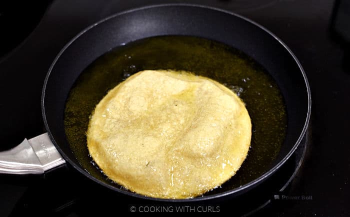 Corn tortillas cooking in oil in a skillet. 
