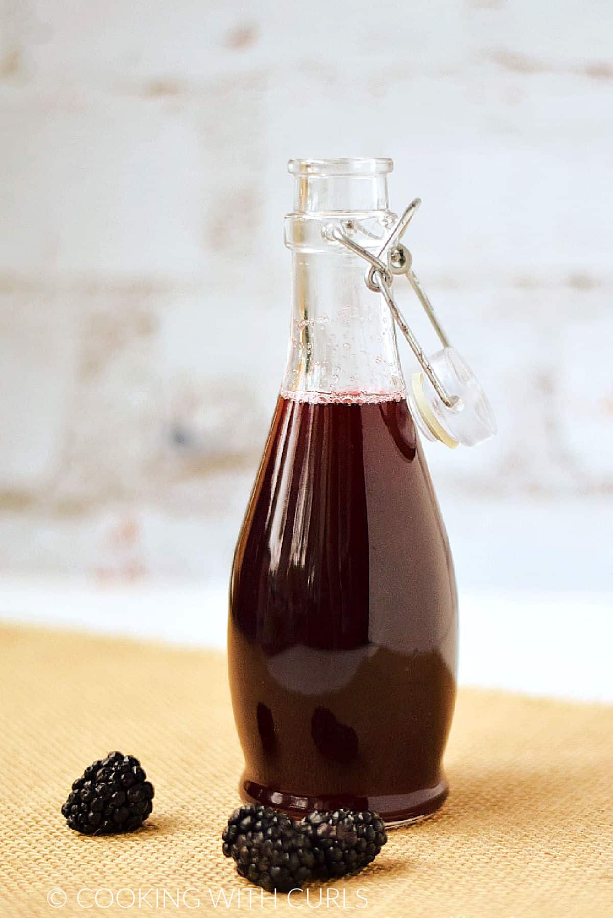 Blackberry syrup in a glass bottle with a swing top lid and fresh berries on a grass napkin.