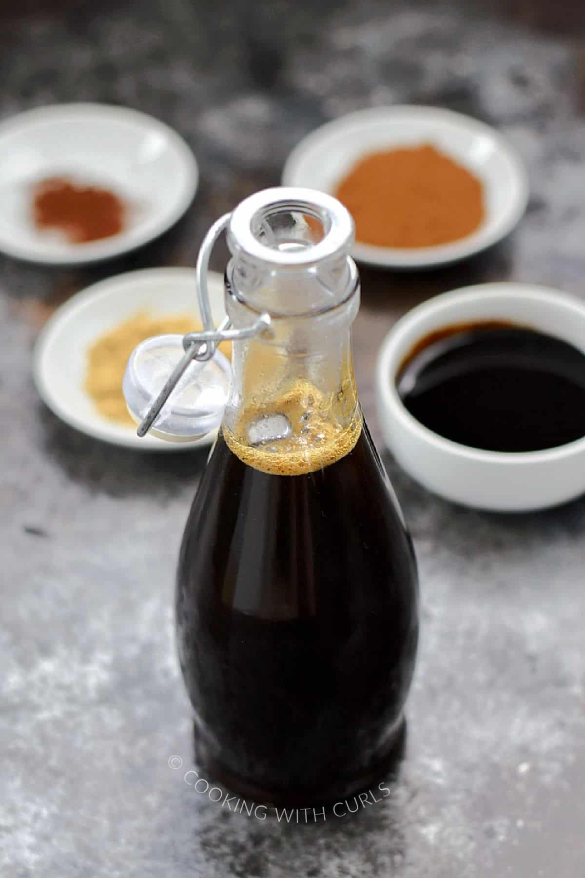 Gingersnap Syrup in a glass bottle with small bowls of spices in the background.