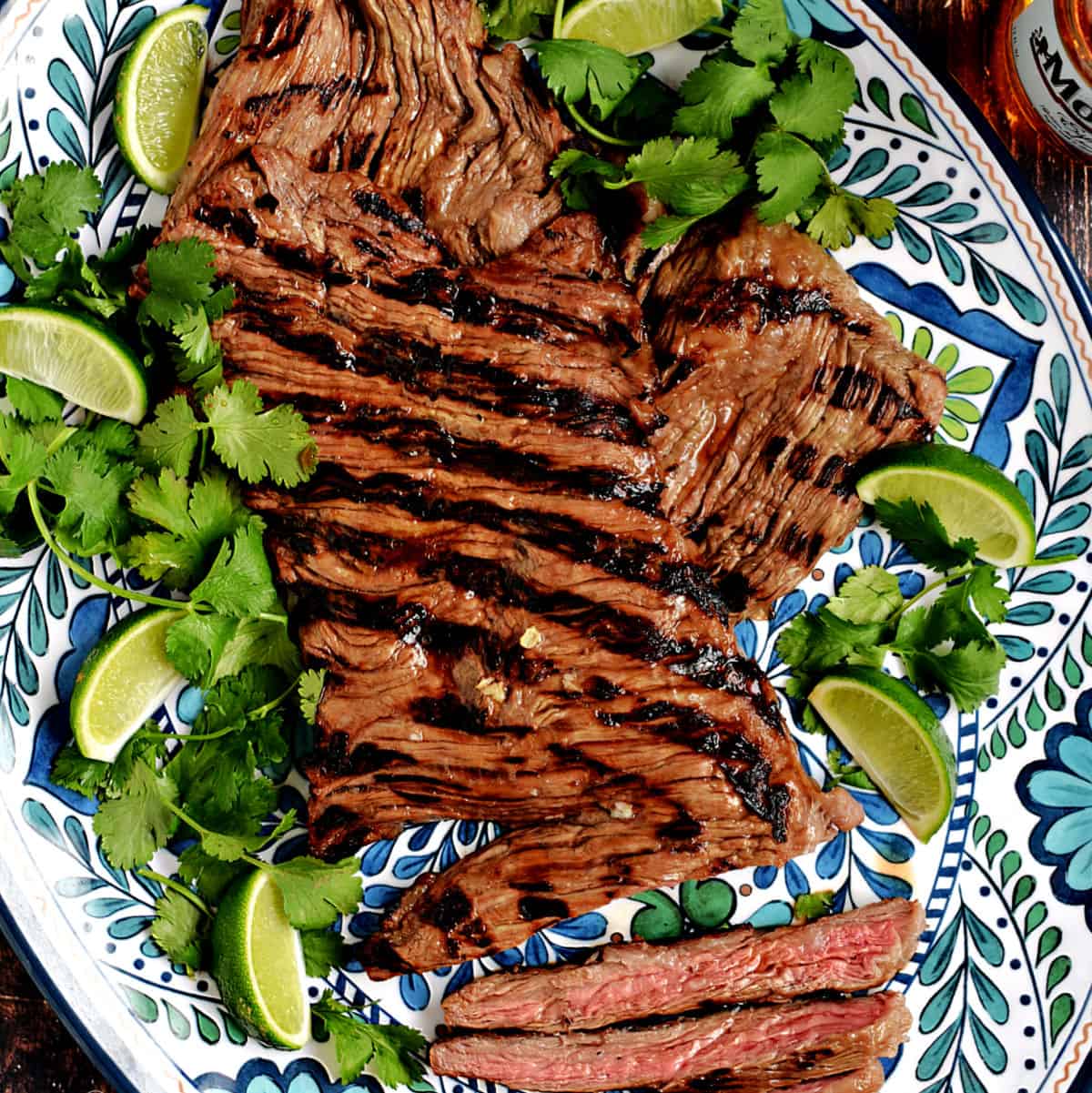 Grilled skirt steak on a platter with lime wedges and cilantro leaves.