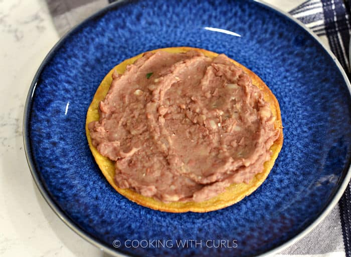 Refried beans spread on a corn tortilla laying on a blue plate. 
