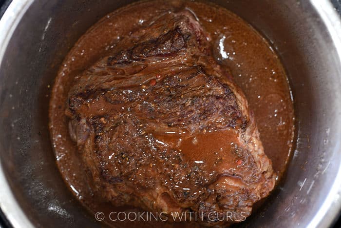 Seared beef in the Instant Pot covered with beef stock and spices. 