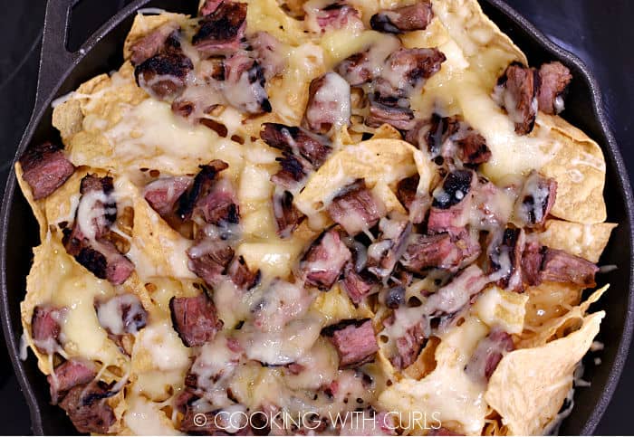 Tortilla chips and steak covered with melted cheese in a cast iron skillet. 