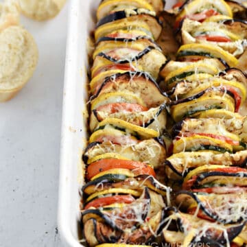 Zucchini, squash, tomatoes and eggplant slices lined up in a white baking dish.
