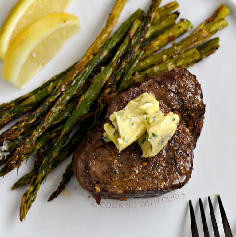 Air Fryer Steak and Asparagus topped with garlic butter on a white plate.