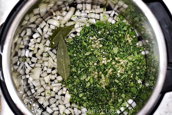 Chopped onions and cilantro, two bay leaves, minced garlic, and water inside a pressure cooker. 