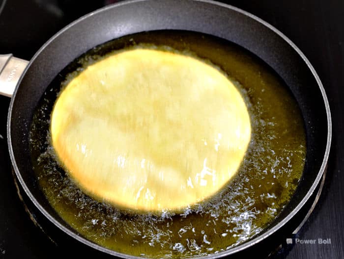 corn tortilla frying in oil inside a small skillet.