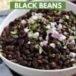 Black beans in a white bowl topped with diced red onion and chopped cilantro with small bowls of rice and crumbled queso in the background and title graphic across the top.