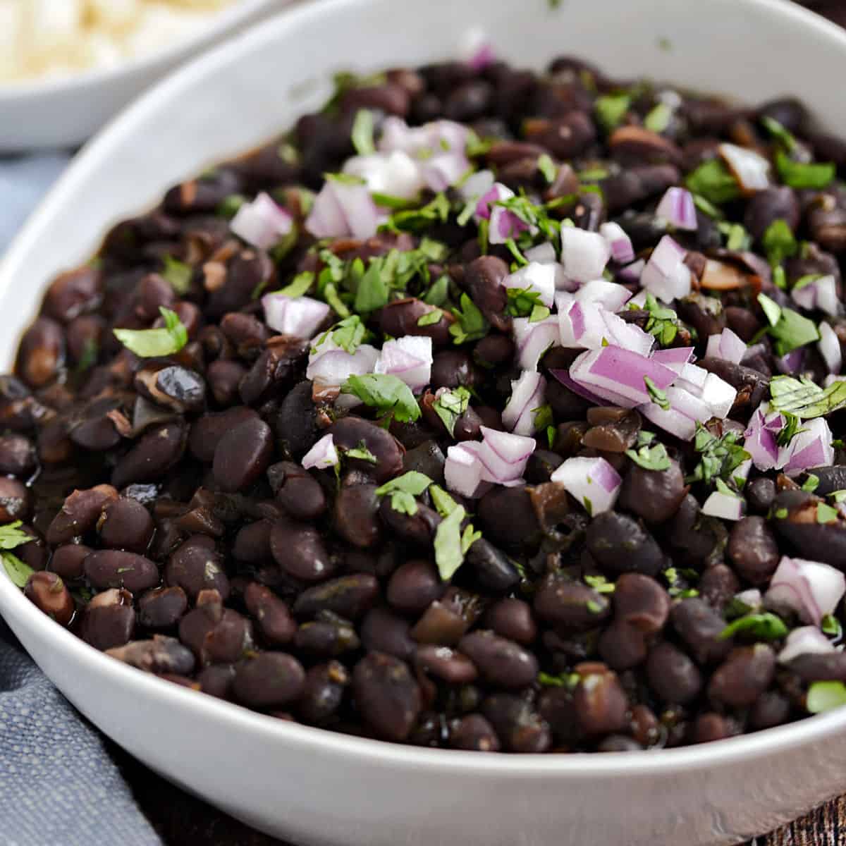 Black beans in a white bowl topped with diced red onion and chopped cilantro.