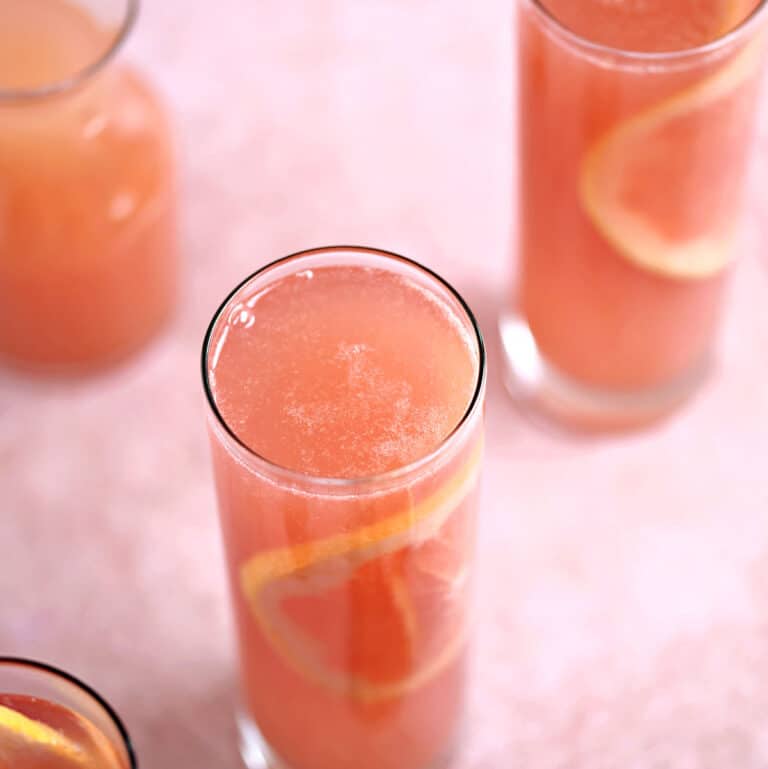 Looking down on three skinny glasses filled with sparkling pink wine, ruby red grapefruit juice with a thin slice of grapefruit in each one.