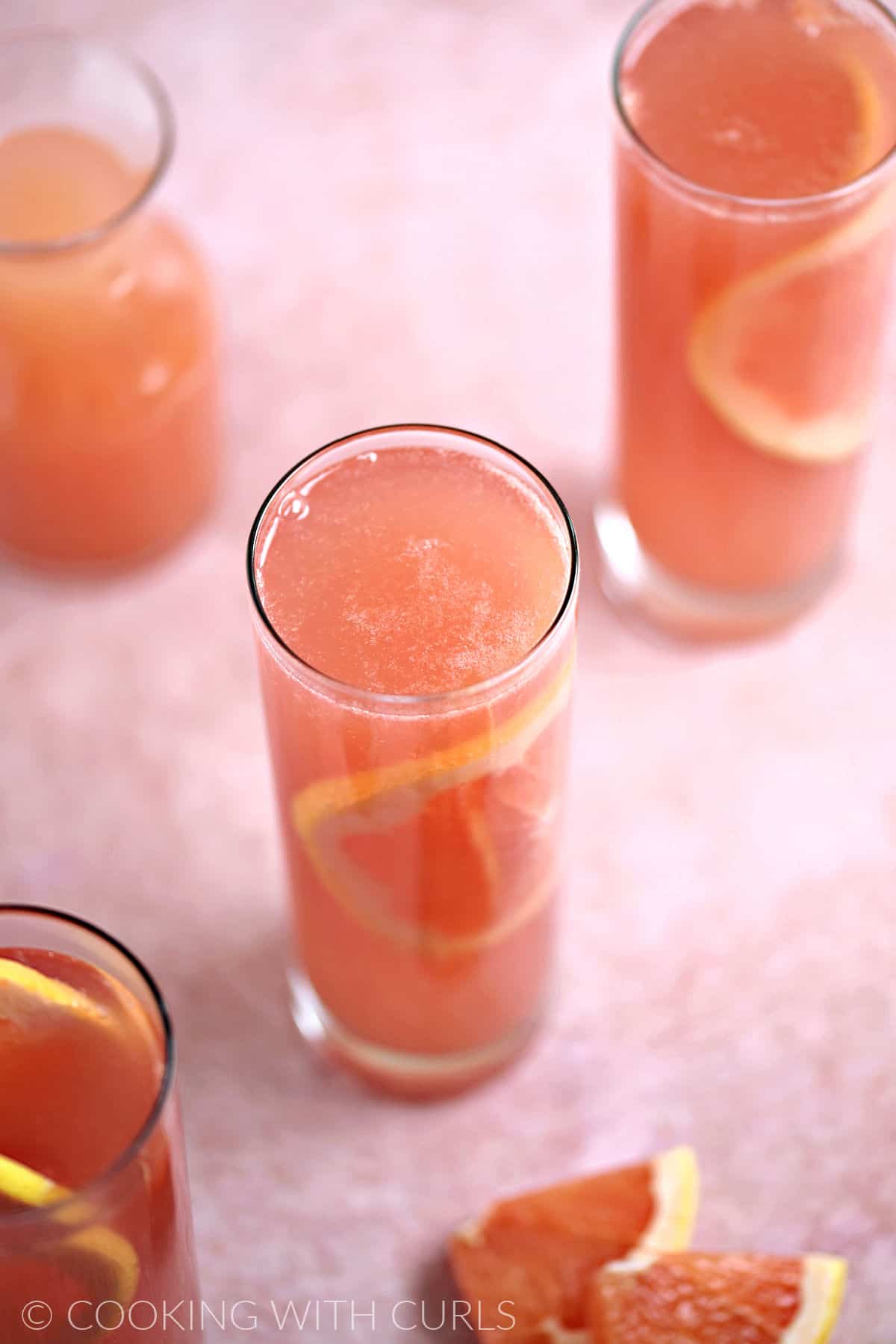 Looking down on three skinny glasses filled with ruby red grapefruit juice, rose champagne, and a thin slice of grapefruit with a carafe of grapefruit juice on the side.