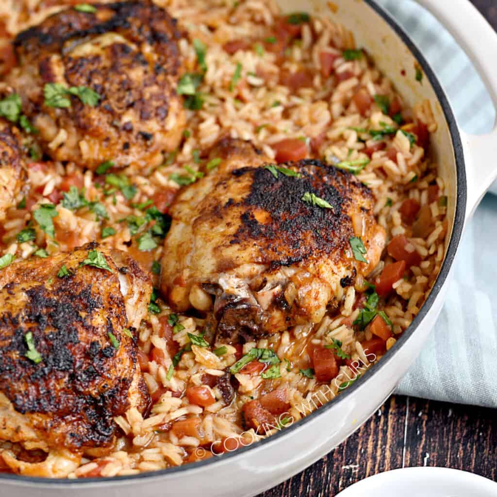 Seasoned chicken thighs on a bed of Mexican rice in a white skillet.