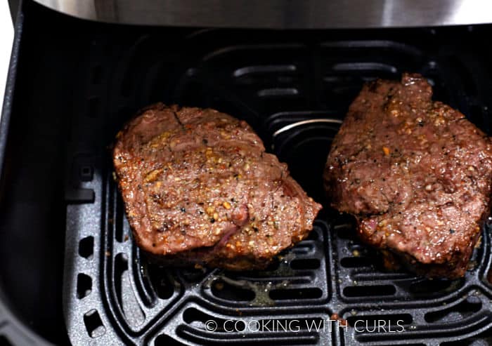 Two cooked steaks in an air fryer basket. 