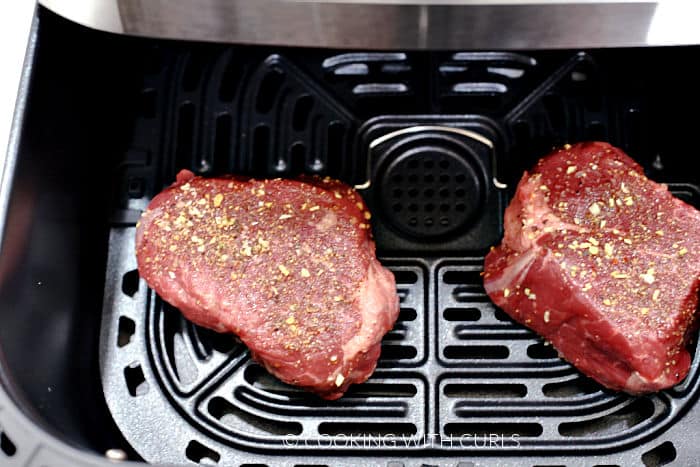 Two seasoned steaks in an air fryer basket. 