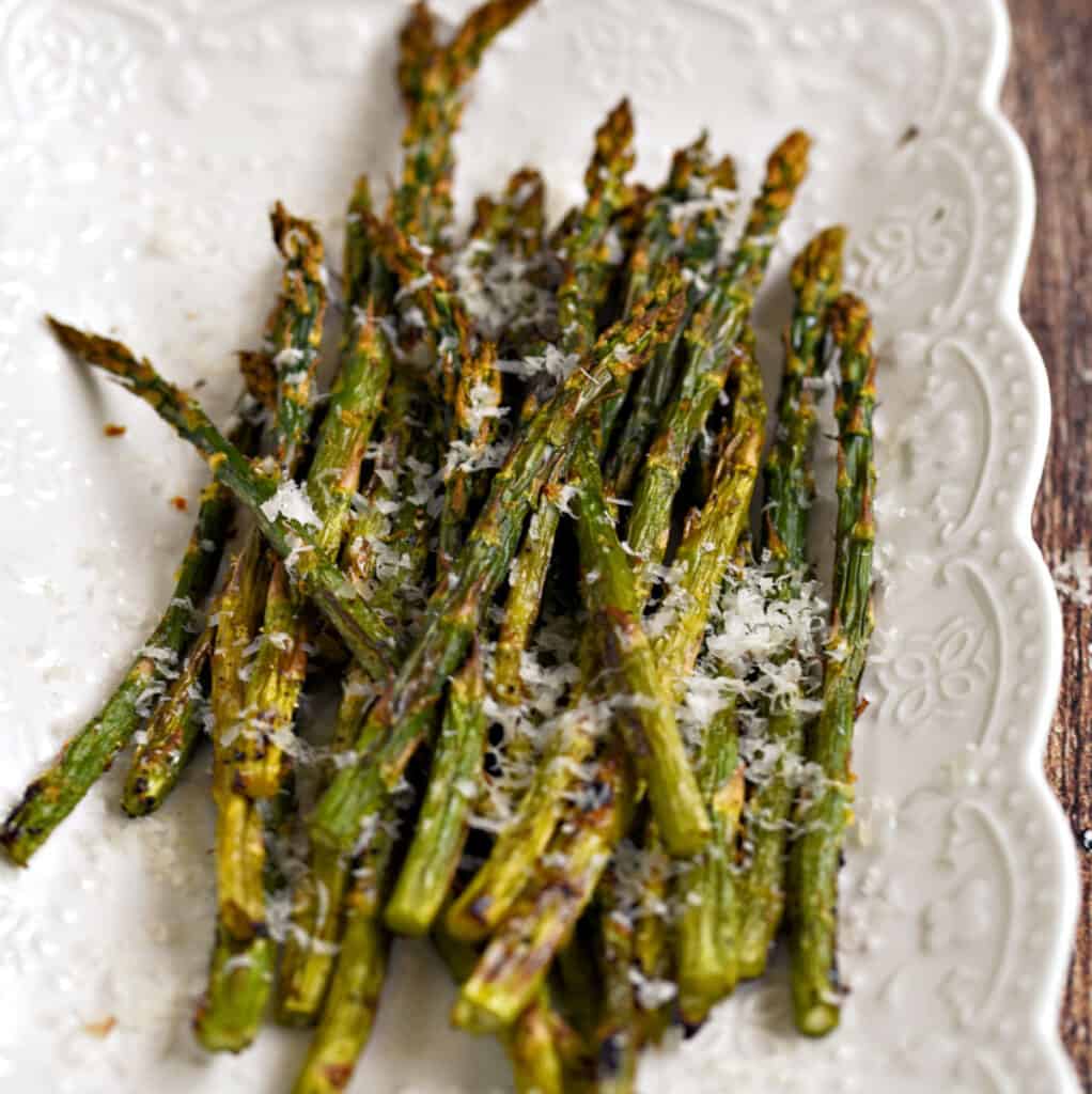 Asparagus spears topped with lemon zest and parmesan cheese laying on a white platter.