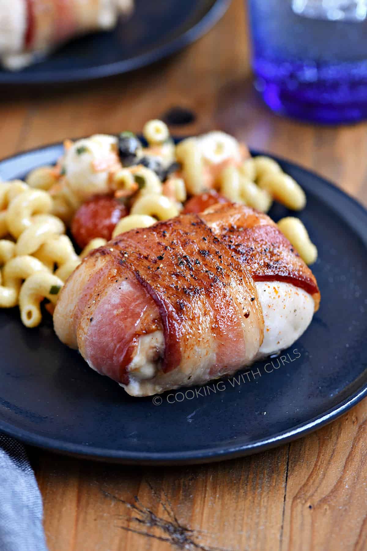 Bacon wrapped chicken and pasta salad on a blue plate.