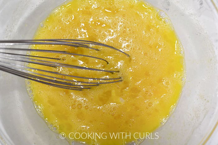 Egg yolks beaten with a whisk in a glass bowl. 