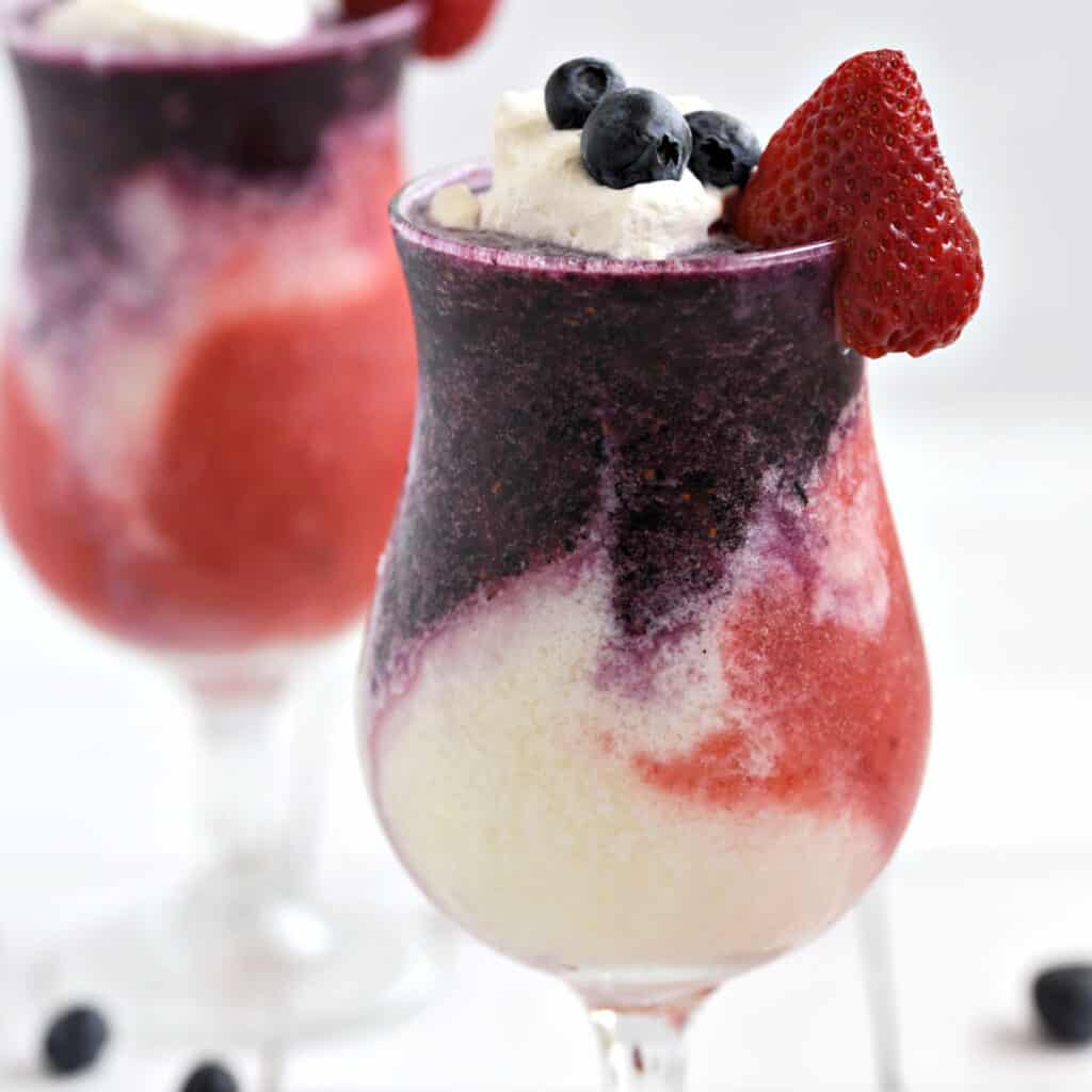 Layered Berry Pina Colada with blue, white, and red layers in two hurricane glasses.