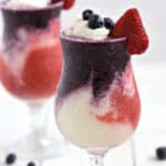 Layered Berry Pina Colada with blue, white, and red layers in two hurricane glasses.