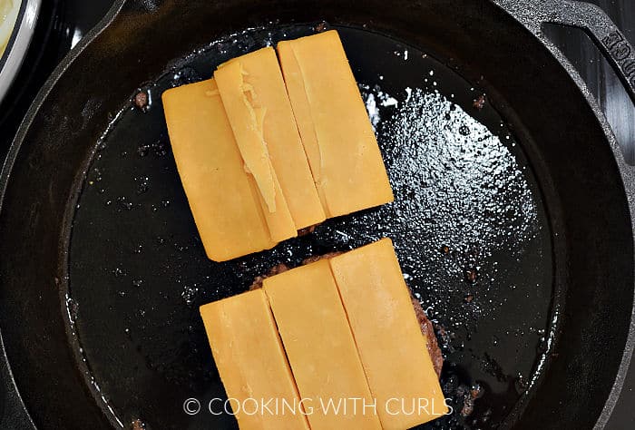 Cheddar cheese slices on top of two burger patties. 