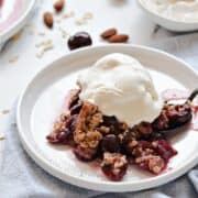 Fresh, baked cherry halves topped with a crunchy oat topping and vanilla ice cream on a small white plate with title graphic across the top.