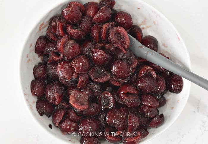 Cherry halves tossed with cornstarch and sugar in a white bowl. 