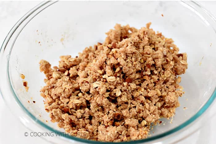 Flour, butter, sugar, almonds, and oats mixed together in a glass bowl. 