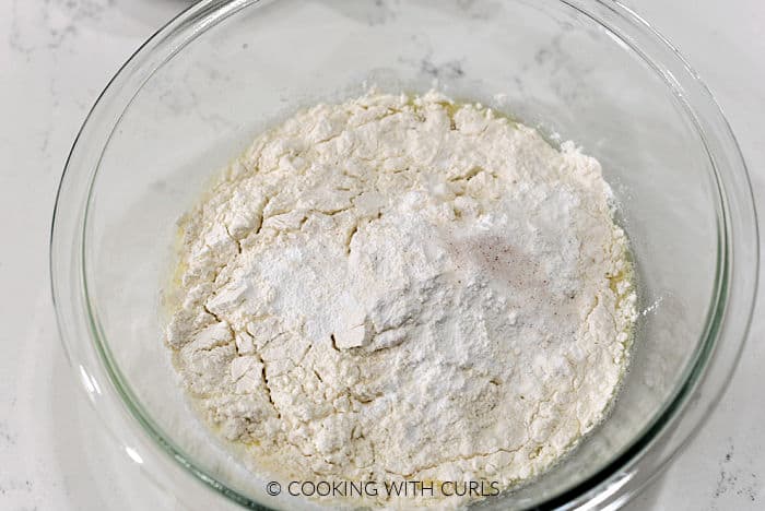 Flour, salt, and baking powder on top of the wet ingredients in a glass bowl. 