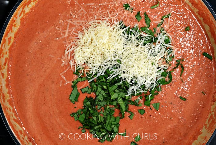 Grated Parmesan and chopped basil added to the vodka sauce in a skillet. 