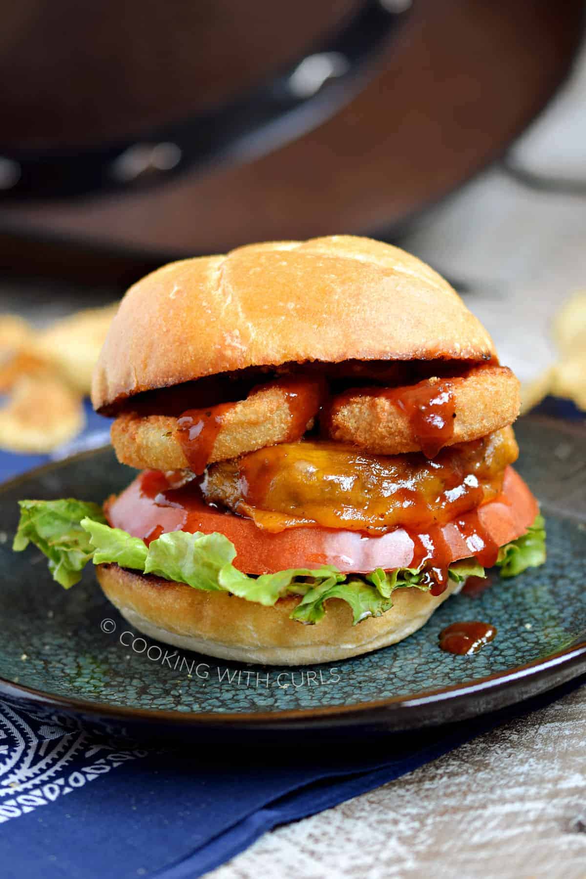 A cheeseburger topped with lettuce, tomato, onion rings, barbecue sauce and a toasted bun.