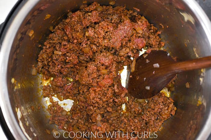 Ground beef mixed with diced onion, garlic, and taco seasoning in a pressure cooker. 