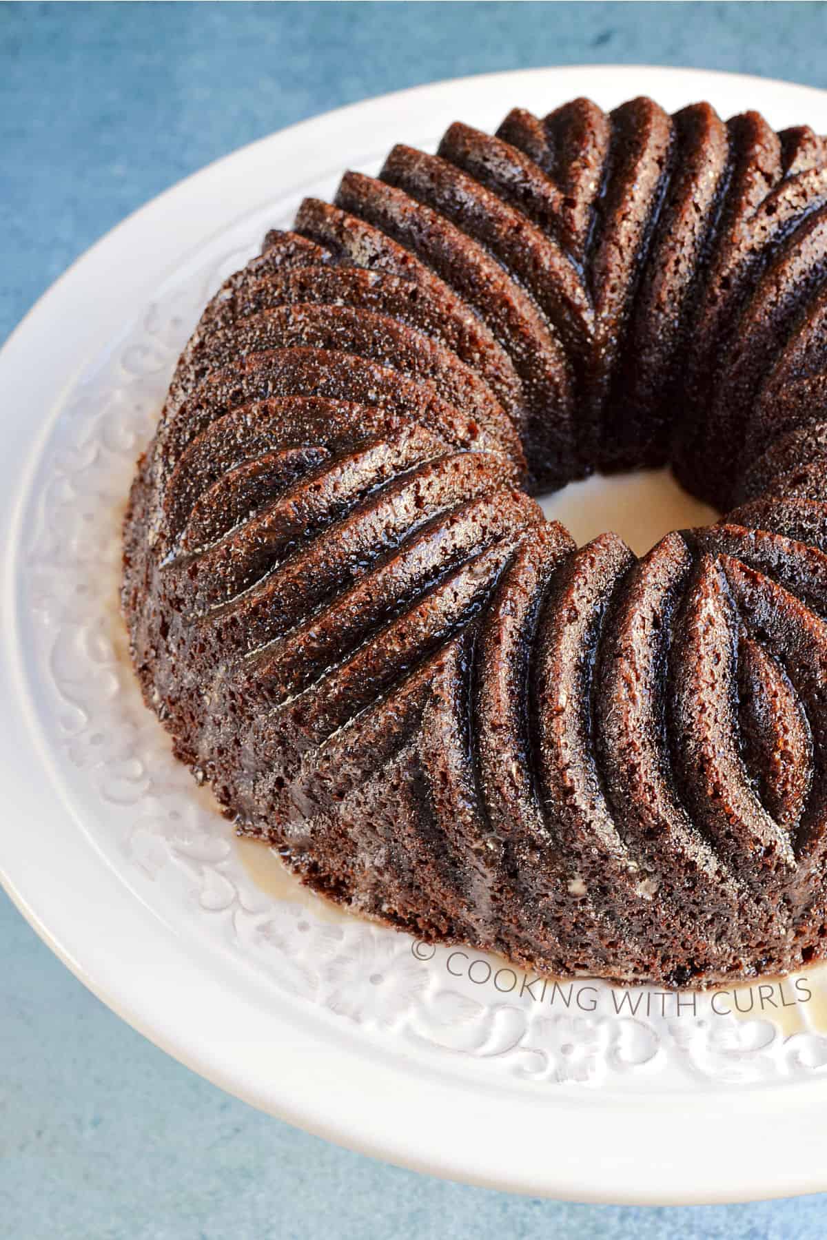 Dark brown bundt cake with decorative design on a white cake plate.