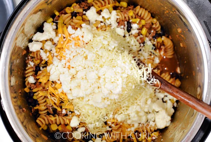 Three types of cheese on top of cooked pasta, corn, and beans. 