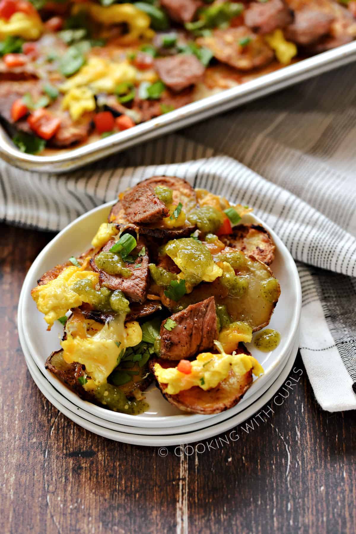 Baked potato slices topped with scrambled eggs, cheese, steak, and salsa verde. 