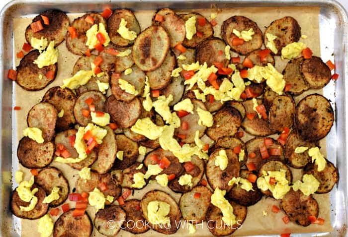 Baked sliced potatoes topped with chopped red pepper and scrambled eggs on a baking sheet. 