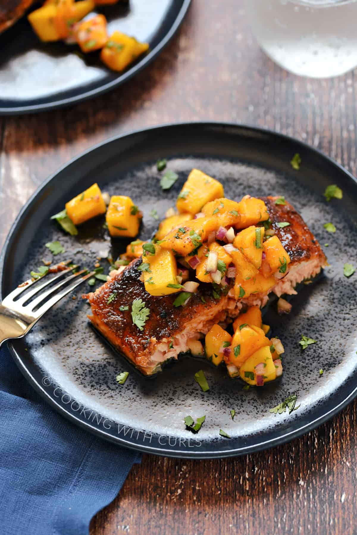 A portion of spice rubbed salmon topped with chopped papaya and mango salsa on a blue plate.