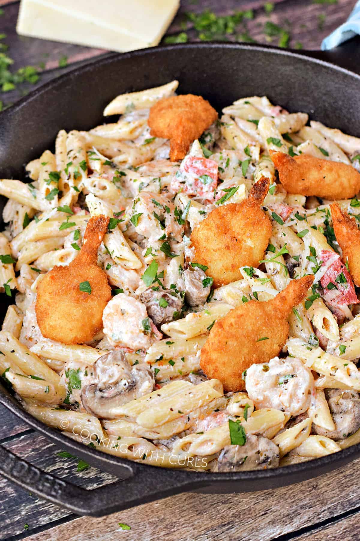 Penne pasta mixed with tomatoes, mushrooms, shrimp, and topped with breaded shrimp in a cast iron skillet.