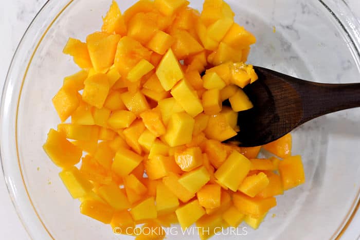 Cubed papaya and mango in a large glass bowl with a wooden spoon. 