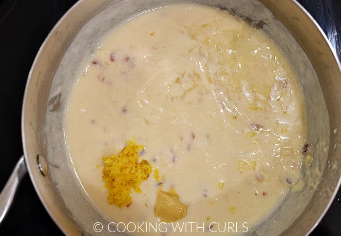 Dijon mustard, lemon zest and juice added to the cheese sauce in a saucepan. 