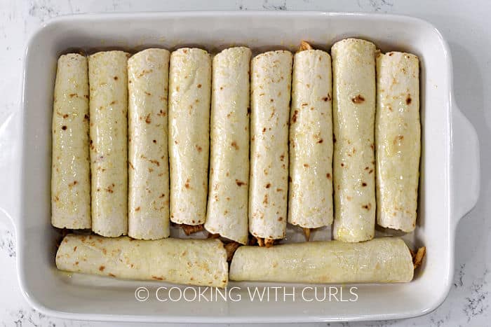 Eleven rolled tortillas lined up in a baking dish. 