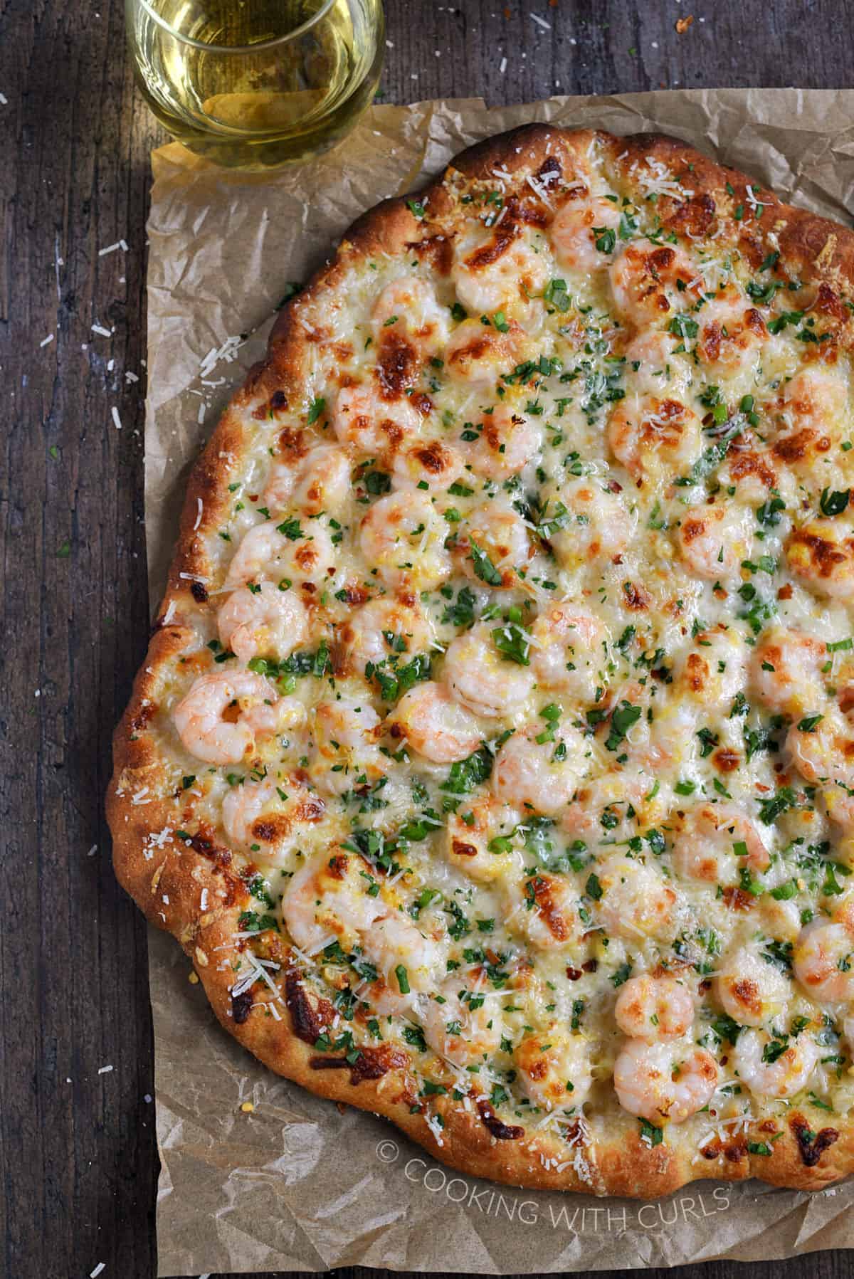 A homemade pizza topped with shrimp, melted cheese ,and chopped parsley on a sheet of parchment paper.